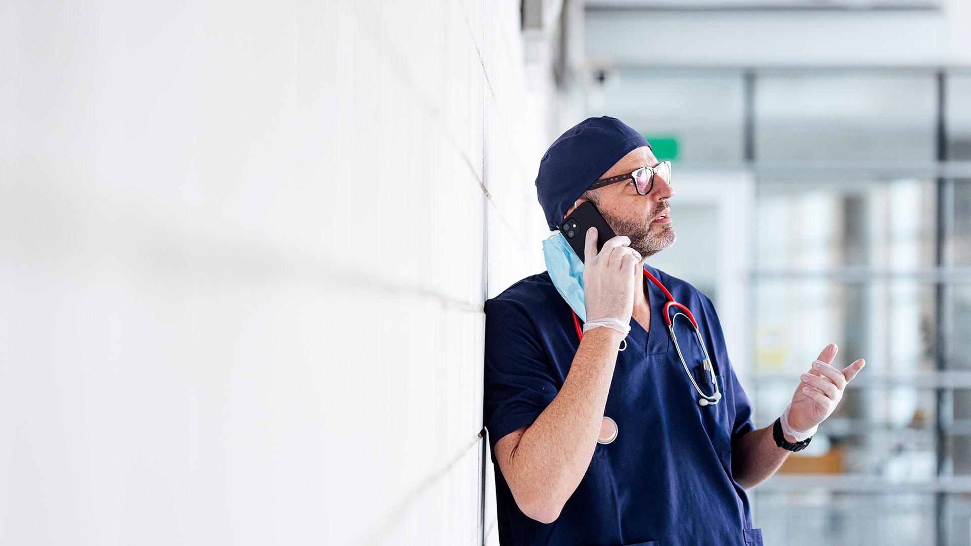 Male doctor in blue scrubs on phone in corridor